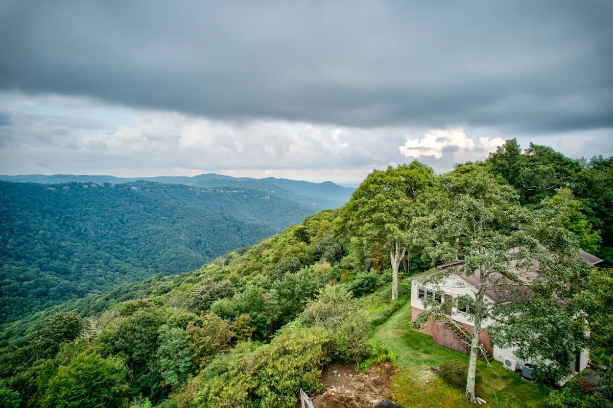 The hero image features a charming single-level mountain home nestled amid lush greenery, set atop a peak with sweeping views of Grandfather Mountain. The spacious porch and expansive deck offer inviting spaces for guests to watch breathtaking sunsets, stargaze on clear nights, or gather for outdoor meals while surrounded by tranquil natural beauty.