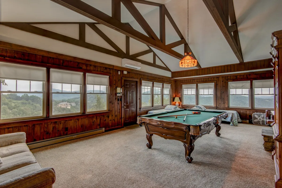 An inviting interior game room with a pool table, large windows framing beautiful views, and rustic wooden features. The mood is casual and relaxed, ideal for laughter-filled evenings and flexible group fun.
