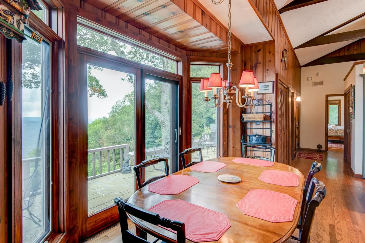 A warm dining area with a wooden table set beneath a chandelier, flanked by large windows that frame sweeping mountain vistas. The space is designed for shared meals and gatherings, with natural light enhancing the welcoming ambiance.