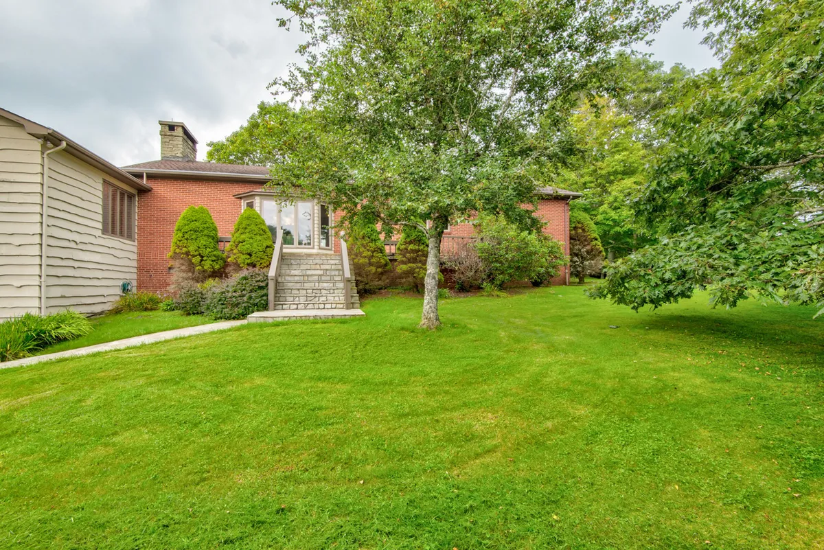 This exterior shot presents the front steps and lush green lawn leading up to the home's entrance, with mature trees providing shade and space for outdoor play. The area invites both casual relaxation and supervised activities for children and pets.