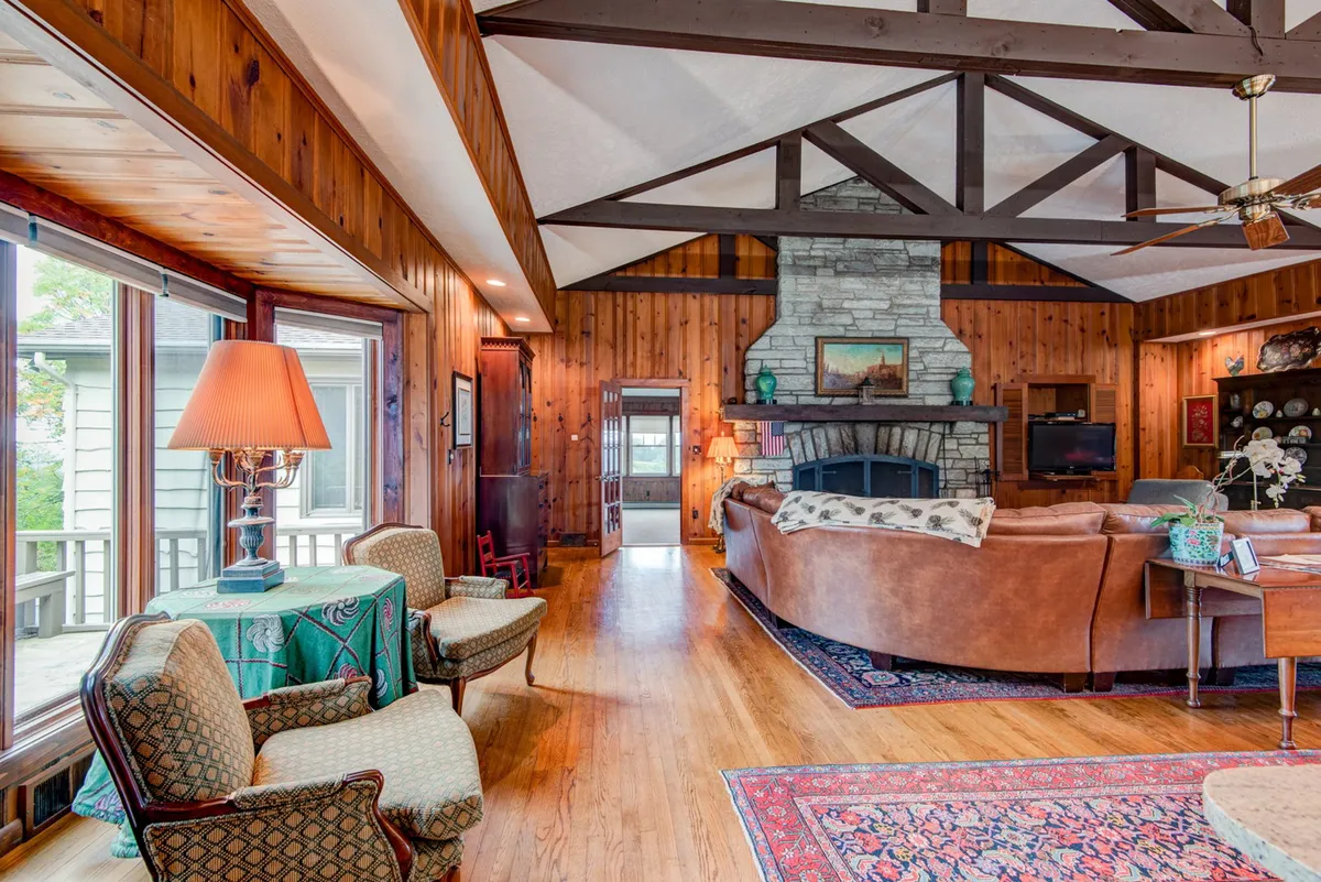 A cozy living area highlighted by a prominent stone fireplace, exposed wooden beams overhead, large windows with breathtaking vistas, and a comfortable, inviting seating arrangement—ideal for both socializing and relaxing by the fire.