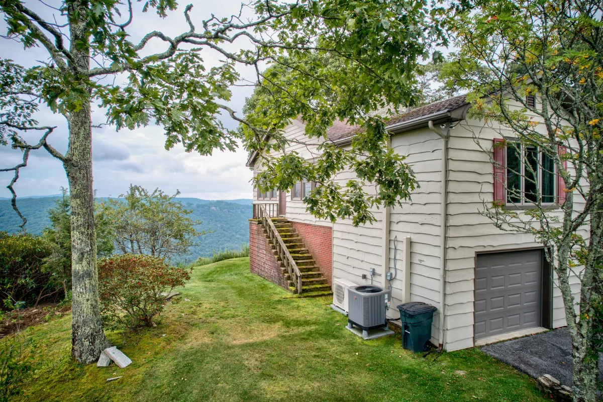This image showcases the exterior of the house, with a staircase leading to the entrance, surrounded by lush greenery and distant mountain views. The porch and natural setting beckon for morning coffee or evening gatherings, as mentioned in the section.