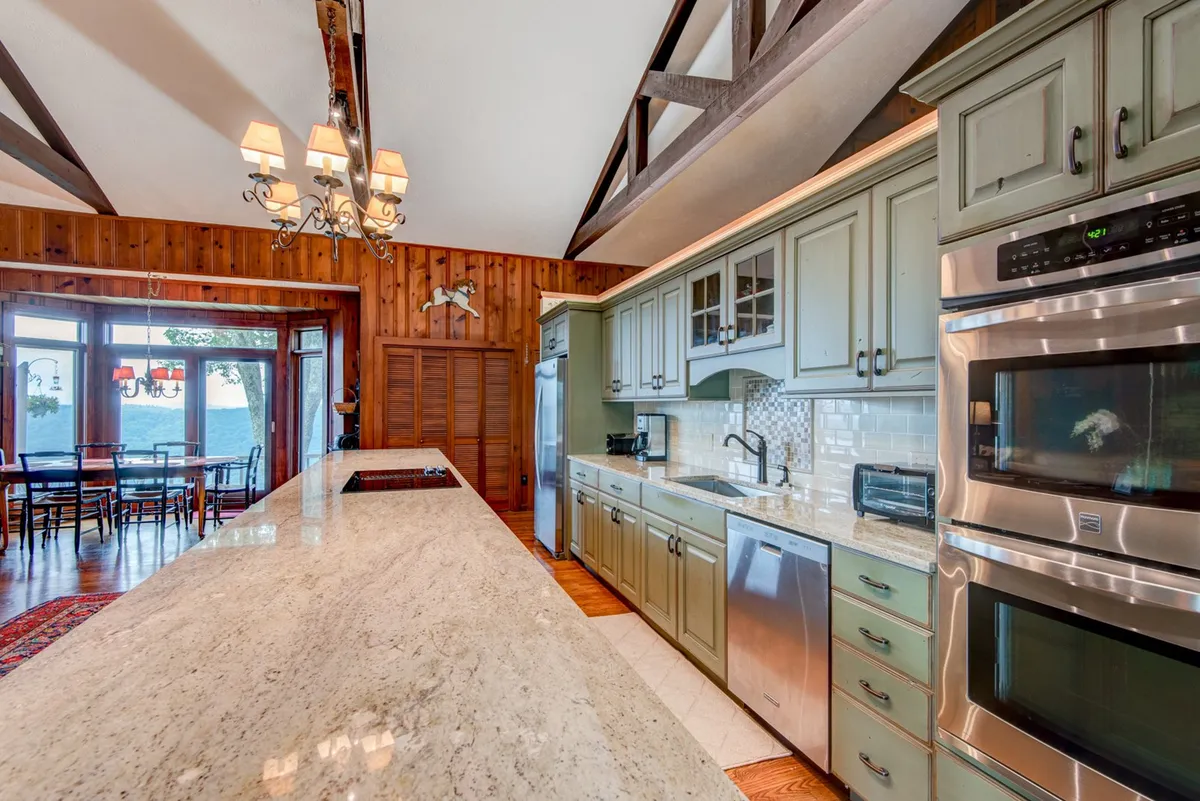 A central view of the kitchen and dining area, featuring a granite countertop, plenty of seating, and large windows. The setup is ideal for family meals, with the dining table adjacent to the kitchen and positioned to enjoy natural light and views.