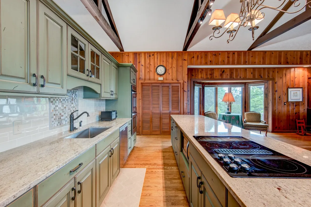 A cozy, open kitchen with a granite countertop island, wooden beams overhead, and expansive windows that offer a clear view of the surrounding mountains. The kitchen is equipped with modern appliances and there’s ample space for cooking and gathering. The natural light and views make the kitchen feel welcoming and connected to the outdoors.